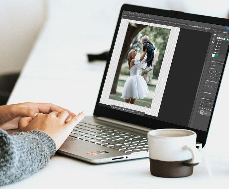 Person using a laptop with photo editing software on a desk with a cup and vase.