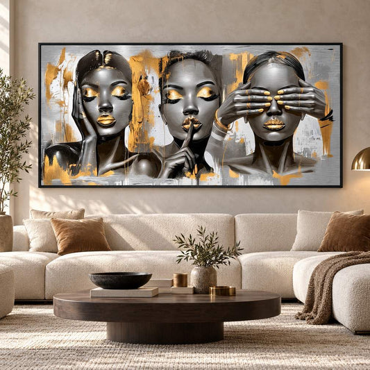 Black-framed metal print of three female portraits with gold accents displayed above a sofa in a living room